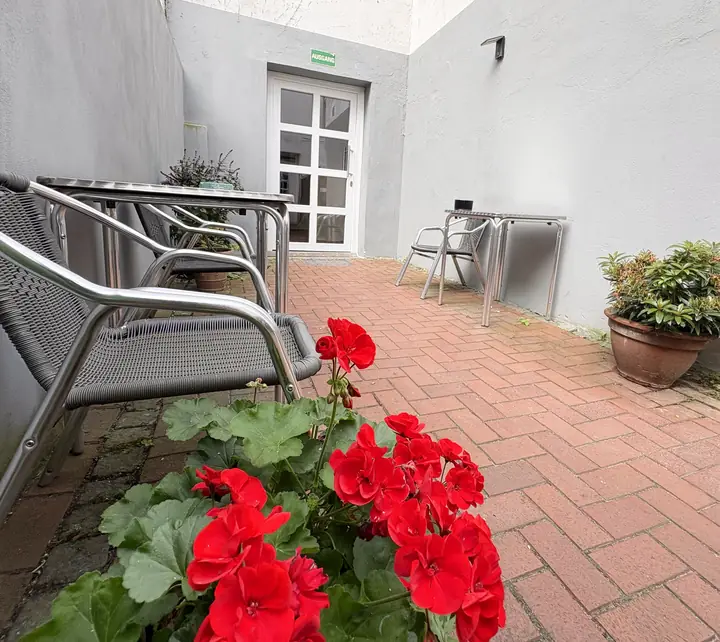 Innenhof mit Tisch, Stühlen, roten Geranien und Klinkerboden