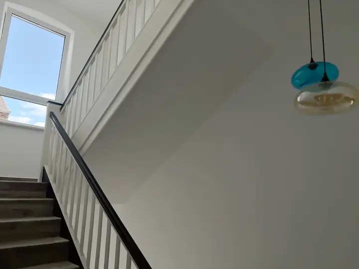 Treppenhaus des Hotels: Holzstufen mit weißem Geländer und dunklem Handlauf, oben ein Fenster