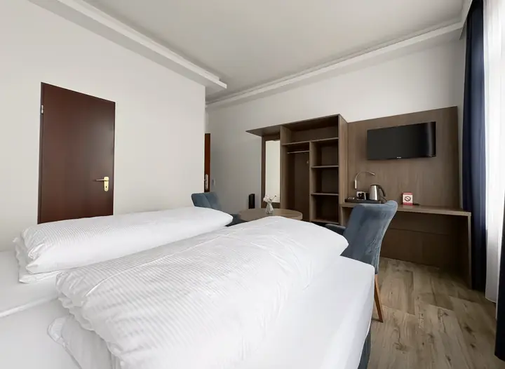 Doppelzimmer in Blau: Betten, offener Schrank, Fernseher und Schreibtisch mit blauem Stuhl