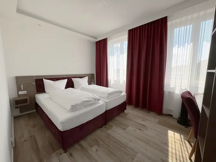 Doppelzimmer in Weinrot: Doppelbett mit weinrotem Rahmen vor roten Vorhängen