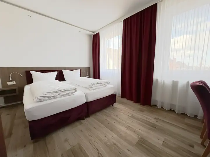 Doppelzimmer in Weinrot: Doppelbett, rote Vorhänge und helle Fenster